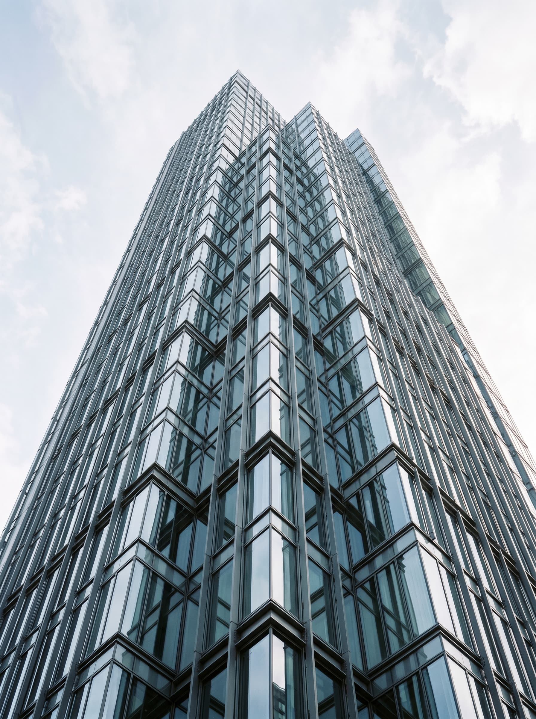 The geometric glass facade of a modern tower seen from below.